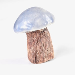 May include: A ceramic mushroom sculpture with a light blue cap and a textured brown stem. The mushroom is a decorative item, likely for home decor, and is set against a plain white background.