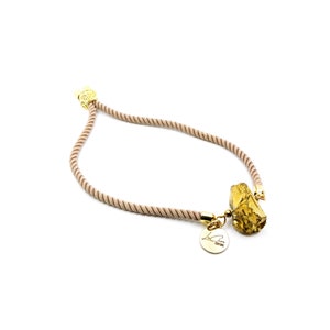 May include: A beige rope necklace with a gold pendant featuring a large, irregular-shaped piece of amber-colored stone. The pendant also includes a smaller, round gold charm with the text "L.A. Couture".