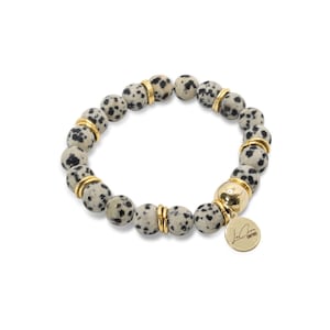 May include: A bracelet made of black and white dalmatian jasper beads with gold accents and a gold charm with the text "La Bien Couture".