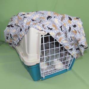 Könnte beinhalten: Ein Haustier-Transportbox mit grau-türkisfarbenem Boden, weißem Oberteil und Drahttür. Die Box ist mit einem grauen Stoff mit einem Muster aus Katzen in verschiedenen Farben bedeckt. Für kleine Haustiere.