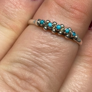 Może przedstawiać: Srebrny pierścionek z rzędem turkusowych kamieni osadzonych w obrączce.