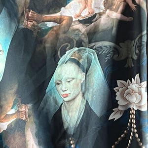 May include: A dark blue fabric featuring a Renaissance-style painting with figures and cherubs. A central portrait of a woman with pale skin, red lips, and a blue veil is visible. A white flower and a pearl necklace are also present.