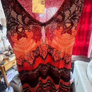 May include: A sleeveless top with a V-neckline, featuring a vibrant mix of colors including red, orange, and black. The top has a keyhole detail at the neckline and a patterned design. The tag reads "FUZZI" and "M".