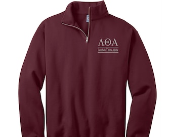 Puede incluir: Una sudadera de color burdeos con cremallera de 1/4 con un logotipo bordado en blanco que dice "ΛΘΑ Lambda Theta Alpha".