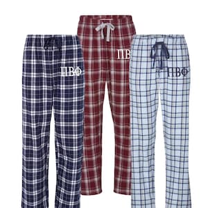 May include: Three pairs of plaid pajama pants with a white embroidered Greek letter design. The pants are in blue, red, and light blue.