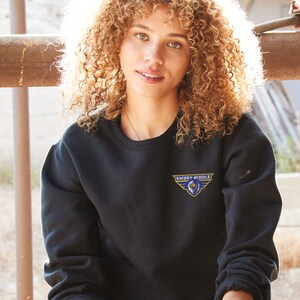 Pode incluir: Uma mulher vestindo uma camisa de moletom preta com um logotipo bordado em azul e amarelo que diz "Embry-Riddle".