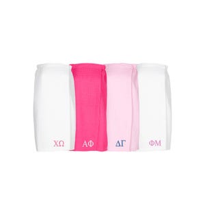 May include: Four white towels with different sorority letters embroidered on them. The letters are XO, AΦ, ΔΓ, and ΦΜ.