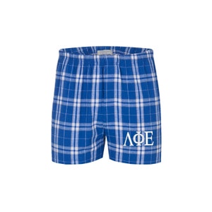 May include: Blue and white plaid pajama shorts with the Greek letters "ΛΦΕ" embroidered in white on the right leg.