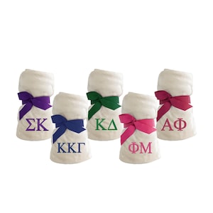 May include: Five white fleece blankets with different colored ribbons and embroidered Greek letters. The letters are: ΣΚ, ΚΚΓ, ΚΔ, ΦΜ, and ΑΦ.