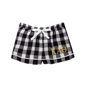 May include: Black and white checkered pajama shorts with a white drawstring and a gold embroidered "KAO" on the right leg.