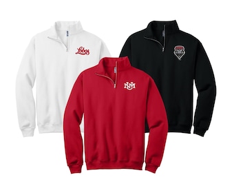 May include: Three quarter-zip sweatshirts in white, red, and black. The white sweatshirt has "Lobos" embroidered on the chest. The red sweatshirt has "NM" embroidered on the chest. The black sweatshirt has a wolf head logo embroidered on the chest.