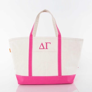 May include: A white canvas tote bag with pink trim and handles. The bag has a large pink embroidered "ΔΓ" on the front.