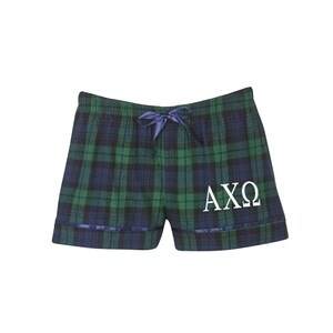 Puede incluir: Pantalones de pijama de cuadros verdes y negros con ribete azul marino y un logotipo "AXO" bordado en blanco.