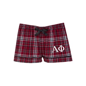 May include: Red and black plaid pajama shorts with a black bow and white embroidered "AΦ" lettering.