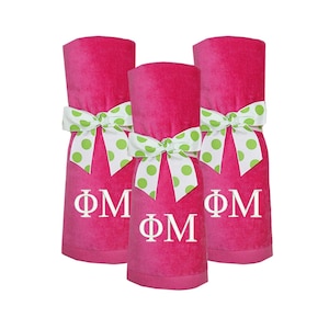May include: Three pink towels with white polka dot bows and the letters "ΦΜ" embroidered on them.