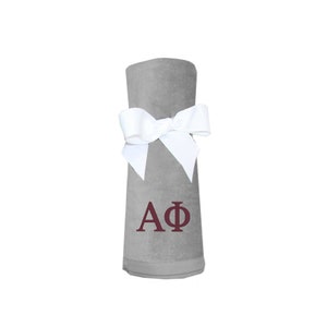 May include: A grey fleece blanket with a white bow and the letters "AΦ" embroidered in maroon.