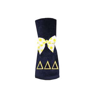 May include: A navy blue towel with a yellow polka dot bow and the letters "ΔΔΔ" embroidered in yellow.