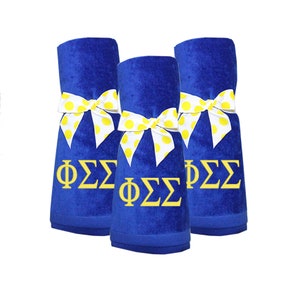 May include: Three blue towels with yellow polka dot bows and the letters "ΦΣΣ" embroidered in yellow.