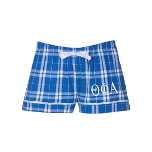 May include: Blue and white plaid pajama shorts with a white ribbon tie and white embroidered Greek letters "ΘΦΑ".