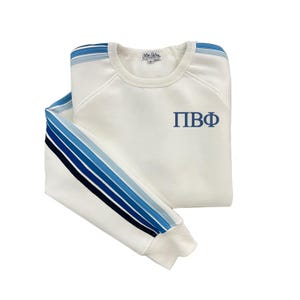May include: White sweatshirt with blue and black stripes on the sleeves. The sweatshirt has the letters "ПВФ" embroidered on the front.