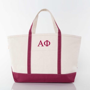 May include: A white canvas tote bag with maroon trim and handles. The bag has a large embroidered "AΦ" in maroon.