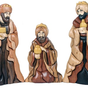 Puede incluir: Tres figuras de madera de los tres reyes magos, cada uno con una túnica de diferente color y sosteniendo un regalo. Los reyes magos están tallados en un estilo detallado con intrincados patrones y texturas.