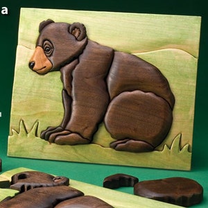 May include: A close-up of a wooden bear cub puzzle. The puzzle is made of different wood types, including black walnut, beech, and maple. The bear is brown and the background is green. The text "Making a Bear Cub Puzzle" is at the top of the image.