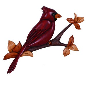 May include: A carved wooden cardinal bird with a crest, perched on a brown branch with three leaves. The bird is a deep red color with a black beak and eye. The leaves are a light brown color.