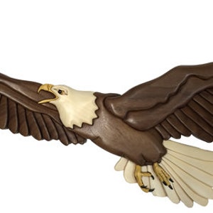 Puede incluir: Una talla de madera de un águila calva en vuelo con las alas extendidas. El águila es marrón con plumas blancas en la cabeza y la cola. La talla es detallada y realista.