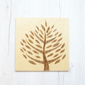 Può includere: Un design di albero bruciato a legno con foglie marroni su uno sfondo di legno chiaro.