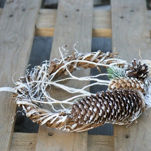 Puede incluir: Una corona de ramas blanqueadas decorada con pi&ntilde;as cubiertas de escarcha blanca.