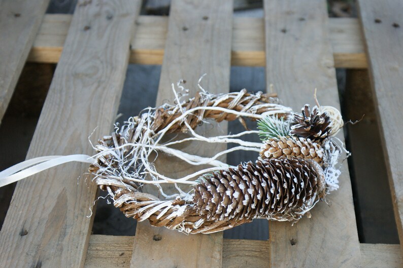 Puede incluir: Una corona de ramas blanqueadas decorada con pi&ntilde;as cubiertas de escarcha blanca.