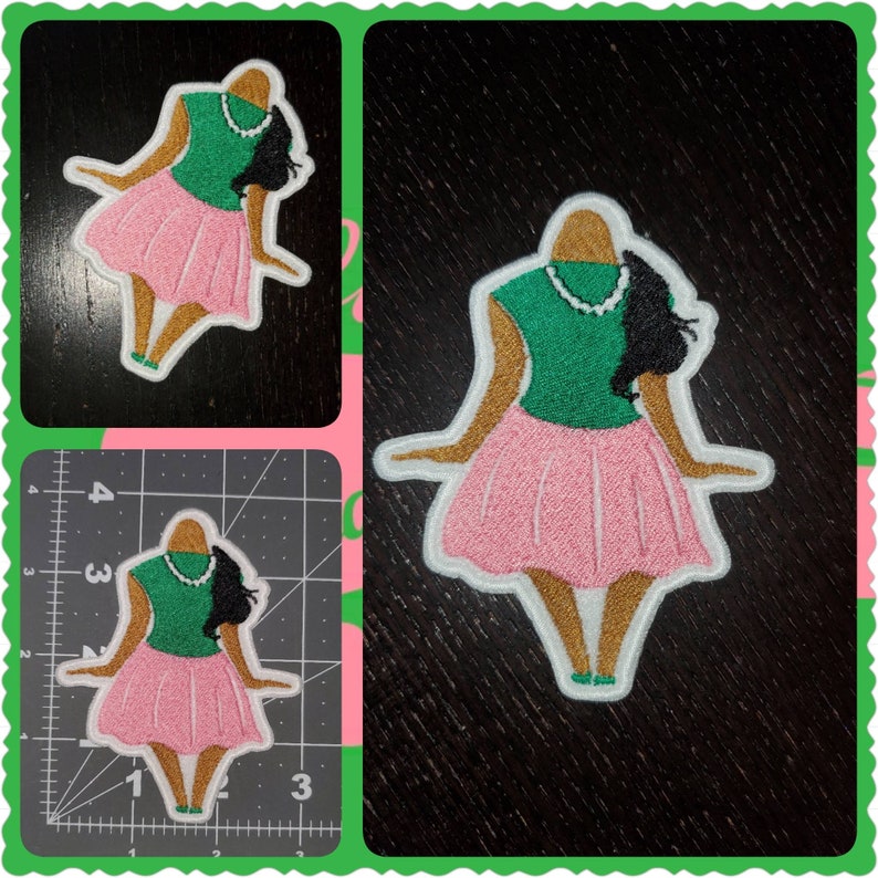May include: Embroidered iron-on patch featuring a cartoon figure of a woman wearing a green shirt, pink skirt, and a pearl necklace. The figure has brown skin and black hair.