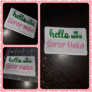 May include: Three white embroidered patches with pink and green lettering. The text on the patches reads "hello my name is Soror Meka".