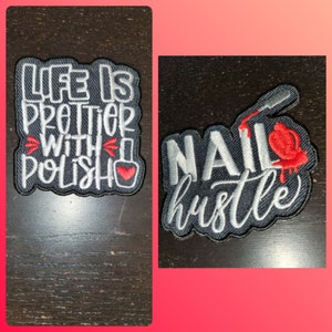 May include: Two embroidered iron-on patches with a nail polish theme. The first patch is black with white text that reads "Life is prettier with polish" and a red heart. The second patch is black with white text that reads "Nail hustle" and a red nail polish bottle with dripping red polish.
