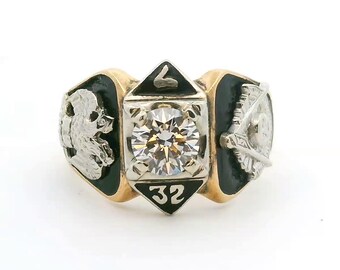 May include: A gold and silver ring featuring a central round-cut clear stone, flanked by black enamel panels. The top and bottom of the center setting display the number 32. One side features an eagle emblem, while the other shows a triangle symbol.