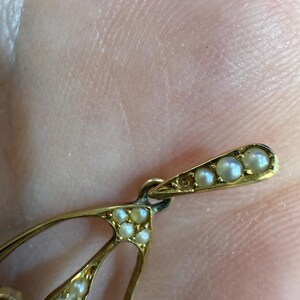 May include: Close-up of a gold-toned pendant with a teardrop design. The pendant is adorned with small, round pearls. The top section features a row of pearls, and the main body has multiple pearls.