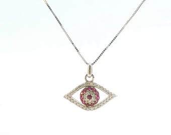 May include: A silver-toned necklace featuring an eye-shaped pendant. The pendant is encrusted with small clear stones along the outer rim and contains a central circular cluster of vibrant pink stones surrounded by a ring of tiny clear stones.