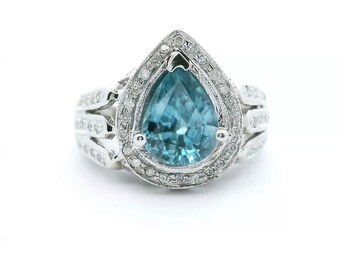 May include: A silver-toned ring featuring a large, pear-shaped, light blue center stone surrounded by a halo of small, clear, round-cut stones. The band is split into three sections on each side, each encrusted with small, clear, round-cut stones.