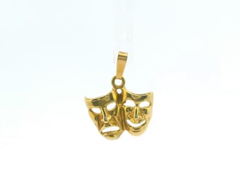 May include: A gold-colored pendant featuring the comedy and tragedy theater masks. The pendant has a polished metallic finish and includes a small vertical loop at the top for attachment to a chain. The design displays two distinct facial expressions.