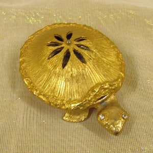 May include: A gold-colored turtle trinket box with a decorative flower design on the lid. The box has a hinged lid and a small opening on the top.