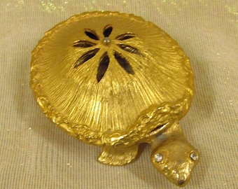 May include: A gold-colored turtle trinket box with a decorative flower design on the lid. The box has a hinged lid and a small opening on the top.