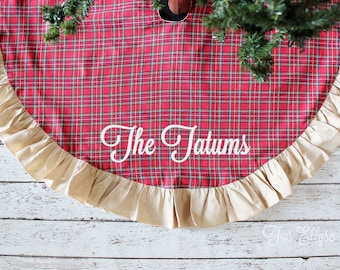 May include: Red and black plaid Christmas tree skirt with a tan ruffled edge. The text "The Tatums" is embroidered in white script across the front. A festive holiday decoration.