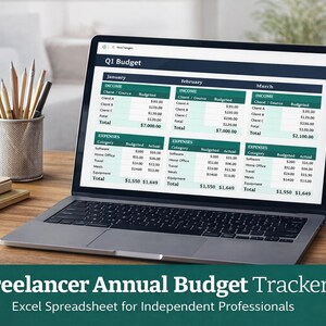 May include: A laptop showing a budget spreadsheet, with pencils in a metal cup and a small potted plant on a wooden desk. The screen displays a financial tracker for freelancers. Text at the bottom reads "Freelancer Annual Budget Tracker".