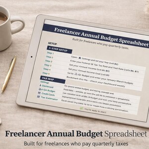 May include: A digital tablet shows a "Freelancer Annual Budget Spreadsheet" with setup instructions and a tab map. A gold pen, a coffee mug, and a notebook are next to the tablet on a neutral-toned surface. The spreadsheet is designed for freelancers.