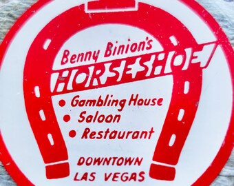 Puede incluir: Cenicero de vidrio rojo y blanco con un diseño de herradura. El texto dice "Benny Binion's Horseshoe", "Gambling House", "Saloon", "Restaurant", "Downtown Las Vegas Nevada".