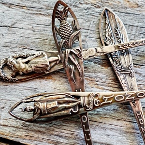 Puede incluir: Tres cucharas de recuerdo de plata vintage con diseños grabados. Las cucharas representan una piña, una bailarina de hula y una palmera. Las cucharas están inscritas con las palabras "Honolulu" y "Hawái".