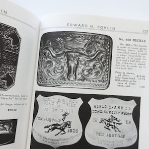 Puede incluir: Una p&aacute;gina de libro abierta con una hebilla de cintur&oacute;n plateada con un dise&ntilde;o de cabeza de toro y dos insignias de campe&oacute;n de rodeo vintage. La hebilla est&aacute; grabada y las insignias tienen texto e ilustraciones de caballos y jinetes.