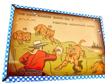 Puede incluir: Un juego de rompecabezas rectangular titulado The Lone Ranger Series-No. 2 Fighting Mountain Lions. El juego presenta una ilustración de dibujos animados de una figura con camisa roja y sombrero blanco apuntando a pumas con puntos.