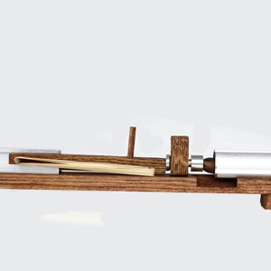 May include: A wooden device with a metal cylinder and a wooden lever. The device is used to roll thin sheets of material, such as paper or fabric.